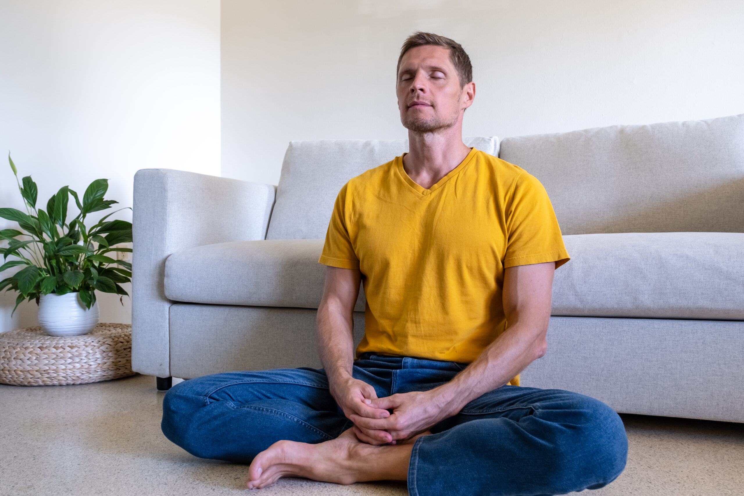 man with eyes closed sitting on floor in Lotus Pose and meditating at home man with eyes closed sitting on floor in Lotus Pose and meditating at home